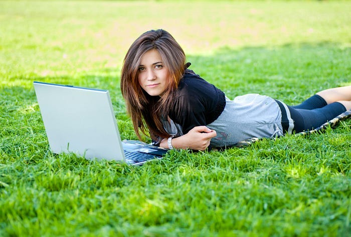 A woman writing on a laptop in the grass. A woman writing on a laptop in the grass.