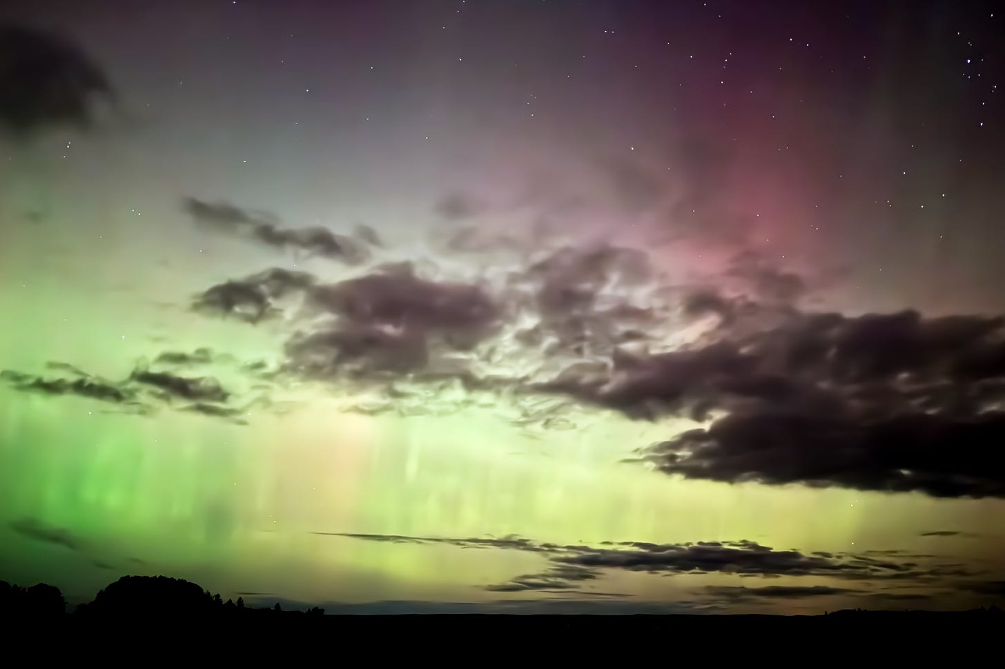 Green and gold aurora bands unfold among night sky clouds.