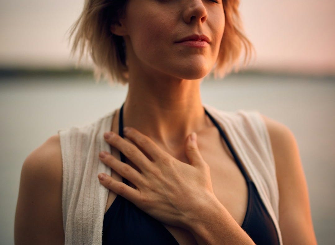 woman in white vest and black bikini with hand on chest