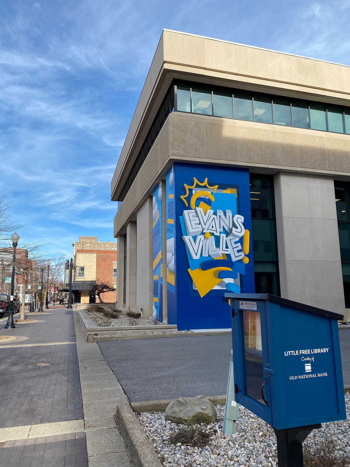 A picture looking down a busy downtown street with a blue and yellow mural with the town name Evansville
