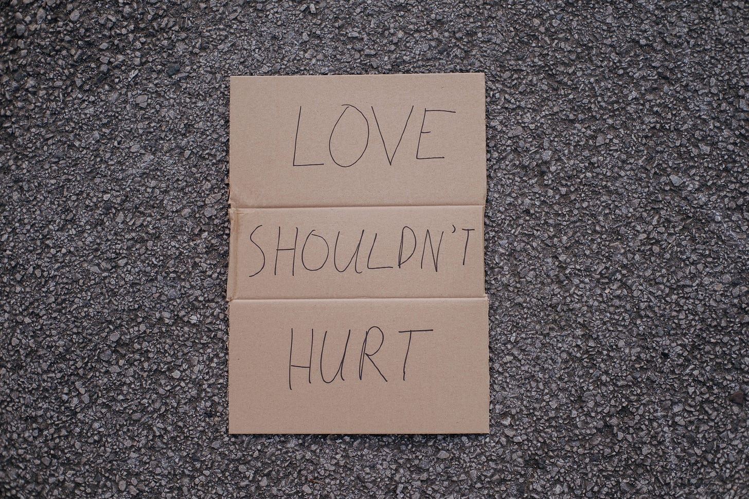 a piece of cardboard has the wrods written "love shouldn't hurt" written on it in black ink