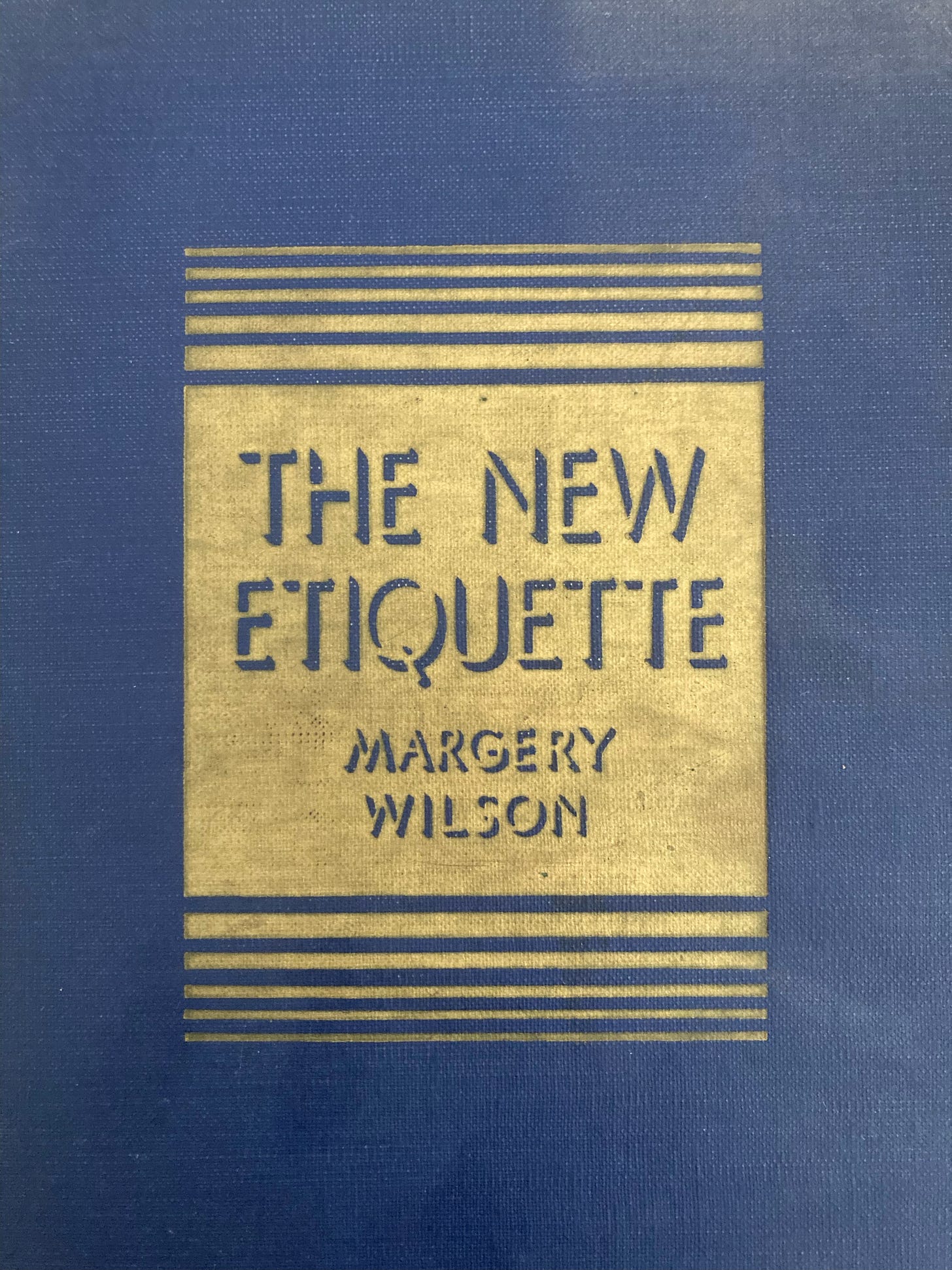 Blue cloth bound book with gold rectangle that has cut out the title and author The New Etiquette Margery Wilson.