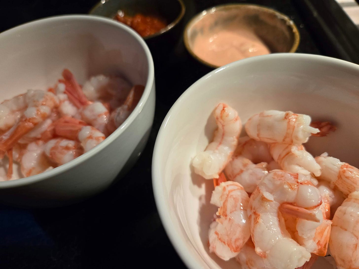 Bowls of poached shrimp with dipping sauces in the background.