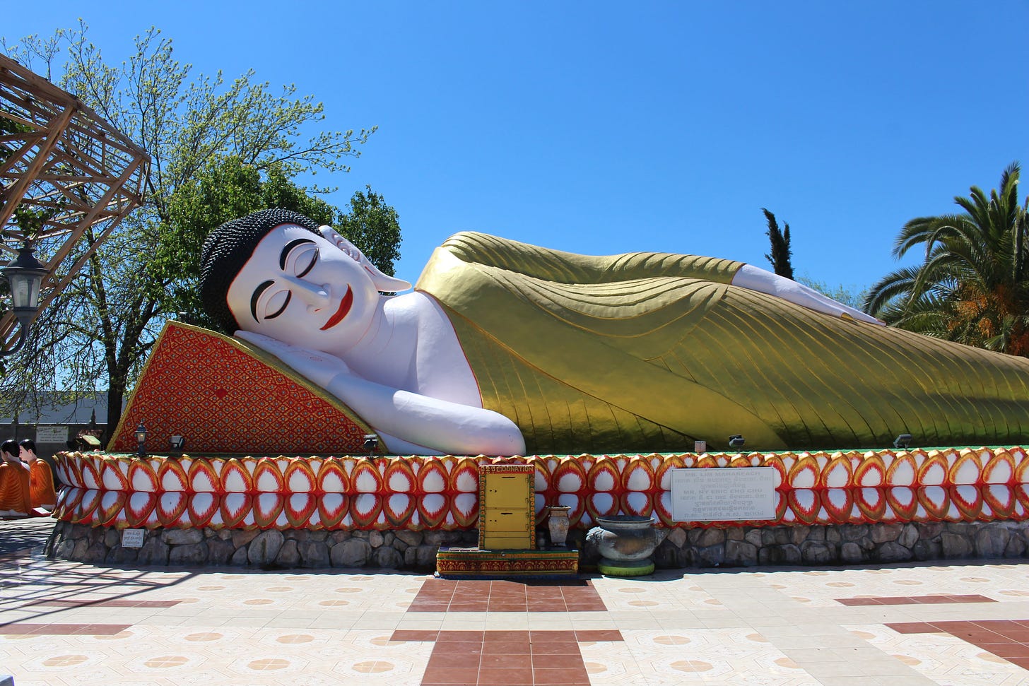 A statue of the sleeping Buddha, who wears a golden robe and rests his head atop a red wedge pillow. 