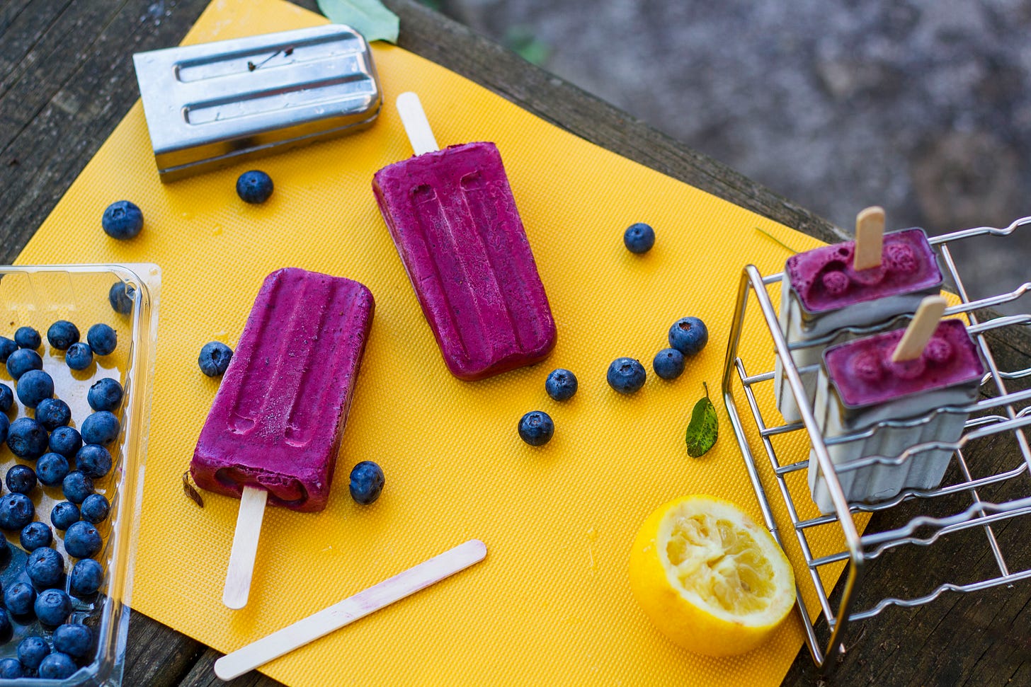 Blueberry popsicles on a yellow cutting board with blueberries and halved lemon