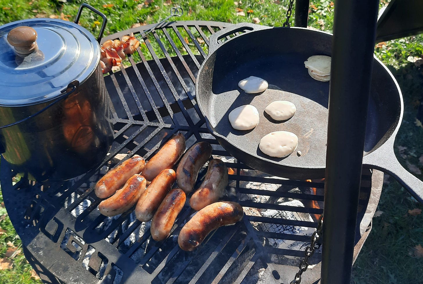 An outdoor firepit with sausages and pancakes cooking
