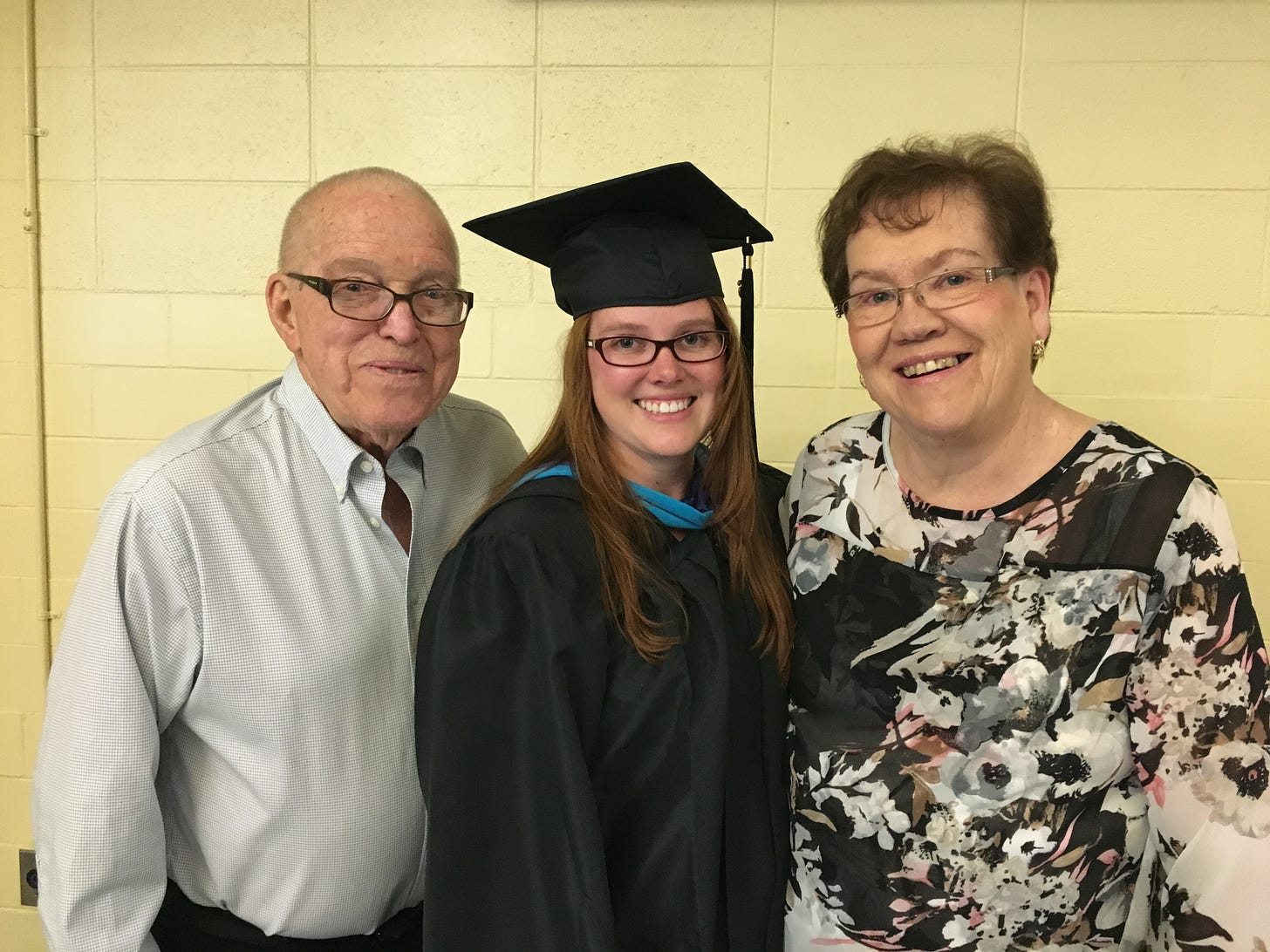 Alyson in graduation attire with her parents on either side, all smiling.