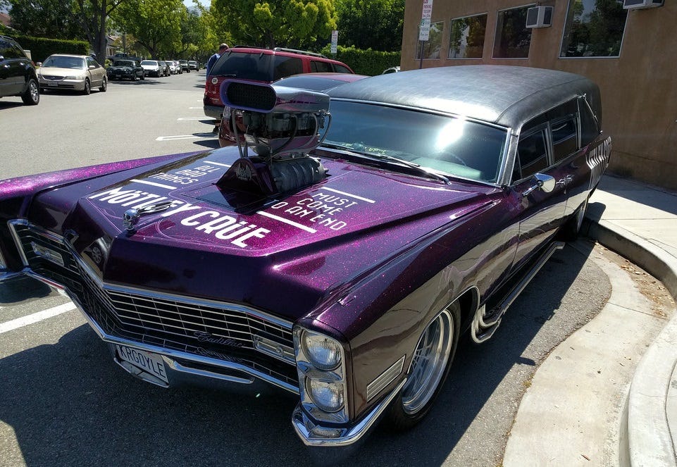 A metallic purple hot rodded Cadillac hearse (from around 1968 or so) with "Motley Crue" in white letters on the hood and sides, with 'All good things must come to an end' also on the hood