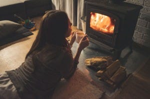 woman lies on stomach in front of fire with a mug of grink, toys in background