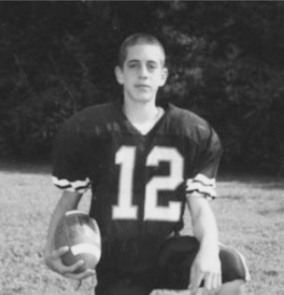 A young, skinny Aaron Rodgers wearing football pads during his teen years