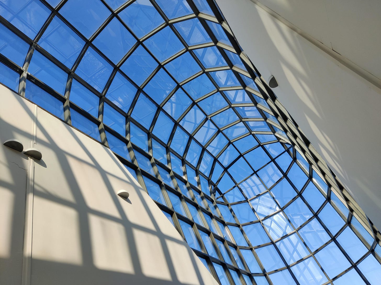 a view of a long corridor the roof of which is glass window panes against a blue sky