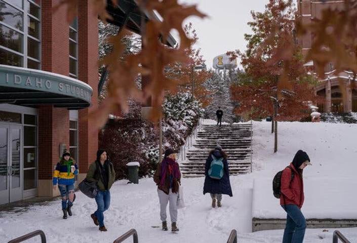 A handful of students wearing winter clothing and carrying backpacks walk on the snow-covered campus of the University of Idaho.
