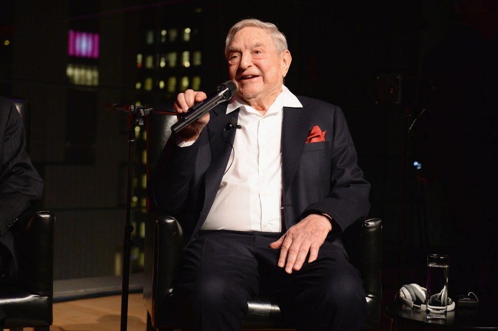 George Soros sitting in a chair holding a microphone