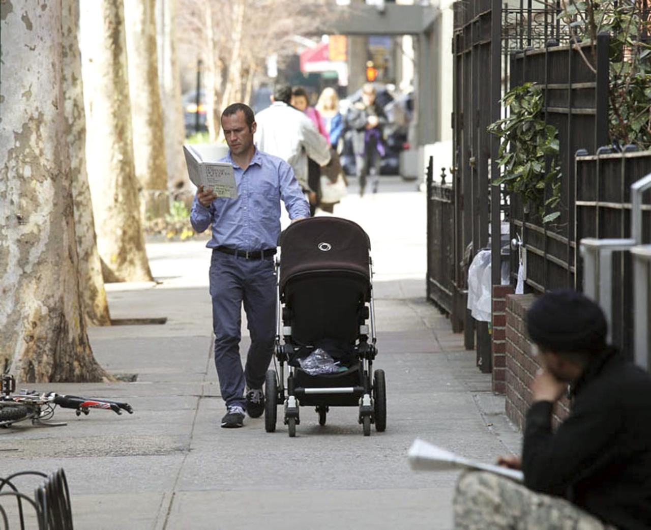 A man reads a book while pushing a stroller on 12th Street near Third Avenue.