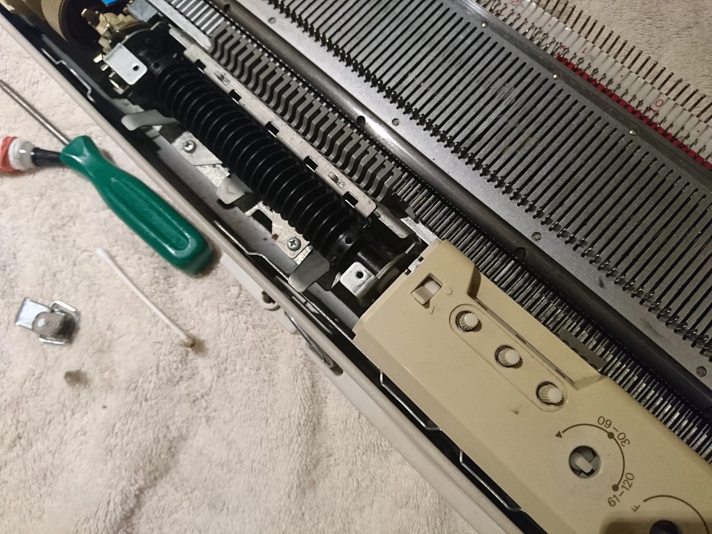 knitting machine with the punch card reader cover removed on a beige towel with a green handled screwdriver nearby