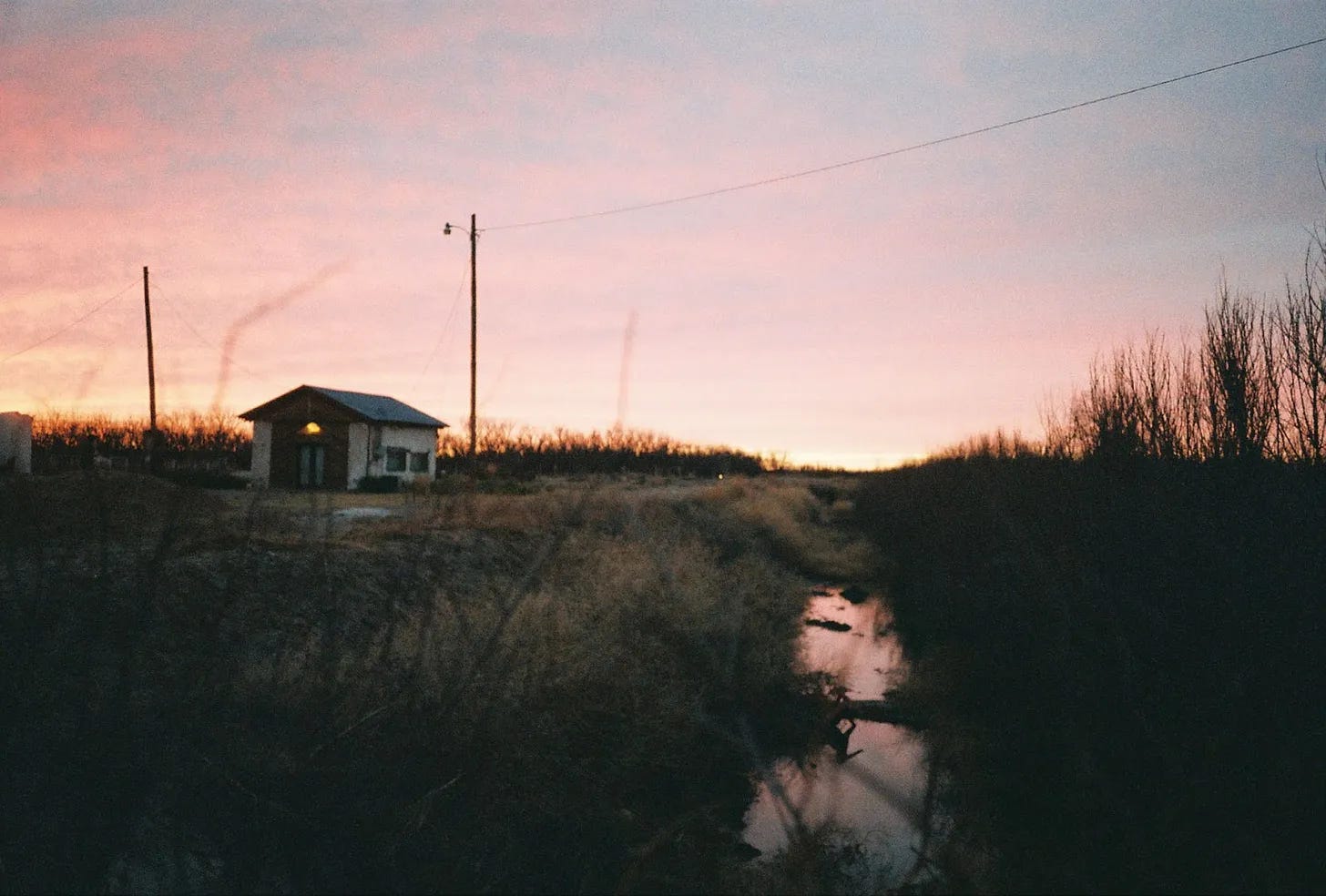 A creek and a small recording studio house backlit by a sunset at Sonic Ranch in Texas.