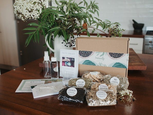 Image of DIY Immunity Remedy Kit with Kit items displayed in front of it - herbs, bottles, recipe cards etc. and boughs from Elder tree in jug behind it. Herbal medicine education made simple and fun for family herbalists and home herbalists. Everyday Empowered