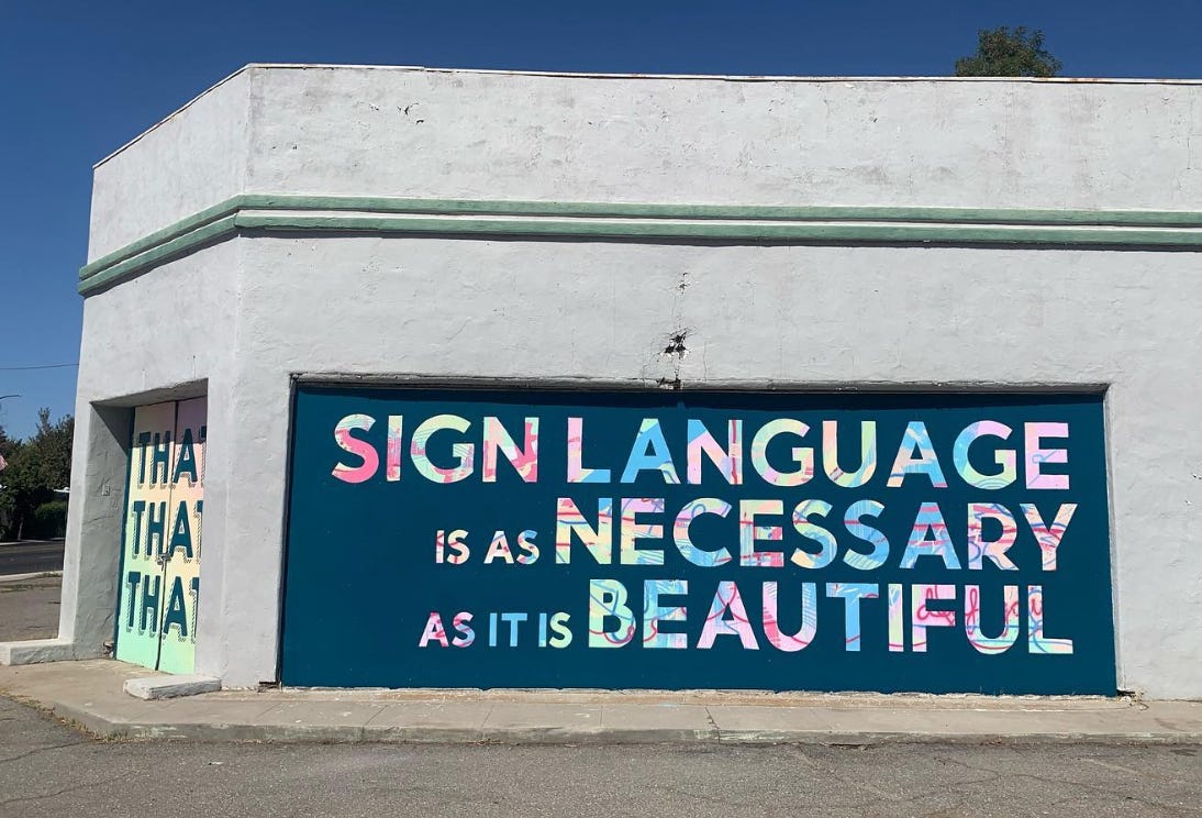 a mural showing colorful text on a dark green/blue background. The text reads “sign language is as necessary as it is beautiful.”