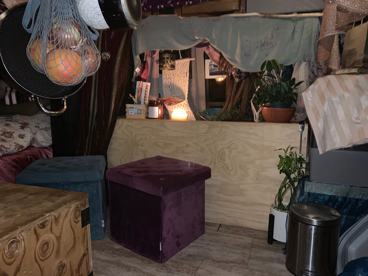The inside of a van, with hanging pots and pans and a produce bag, a lit candle and a box of paints, a mask from Bali and a smattering of plants, and two velvet stools