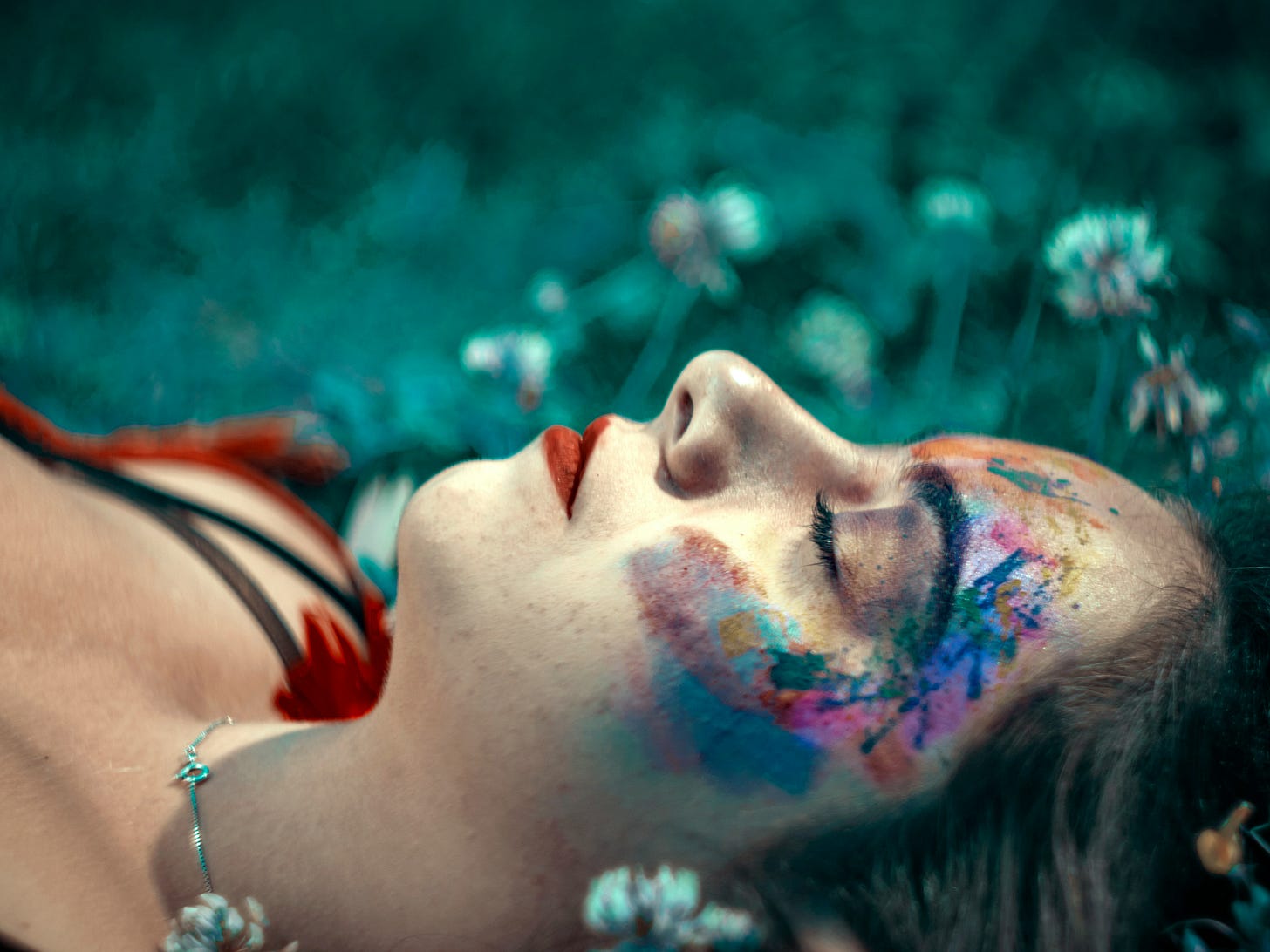 close up of woman with painted face lying on the grass with eyes closed
