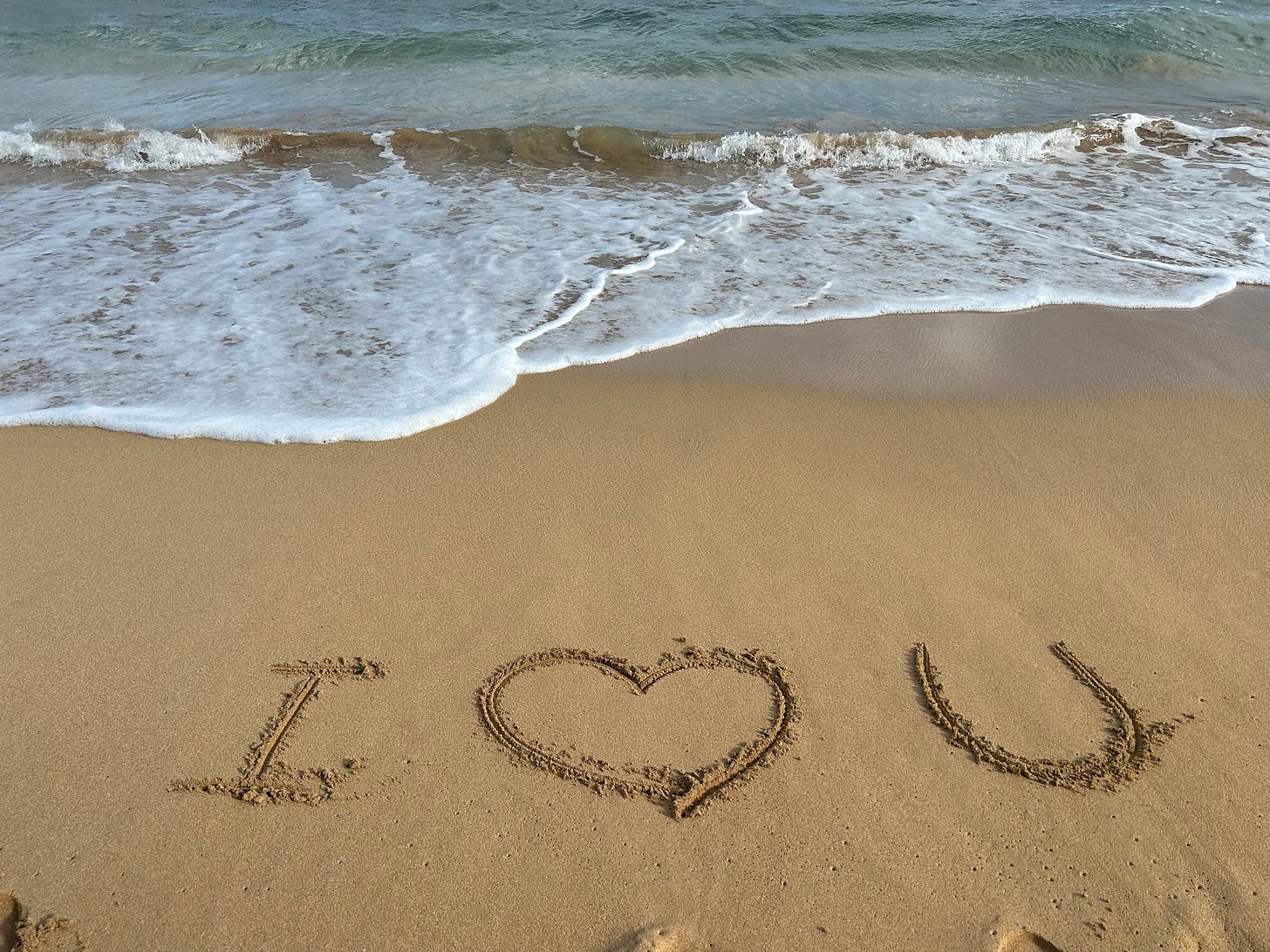 A sandy beach with waves rolling in and "I [heart] you" drawn in the sand