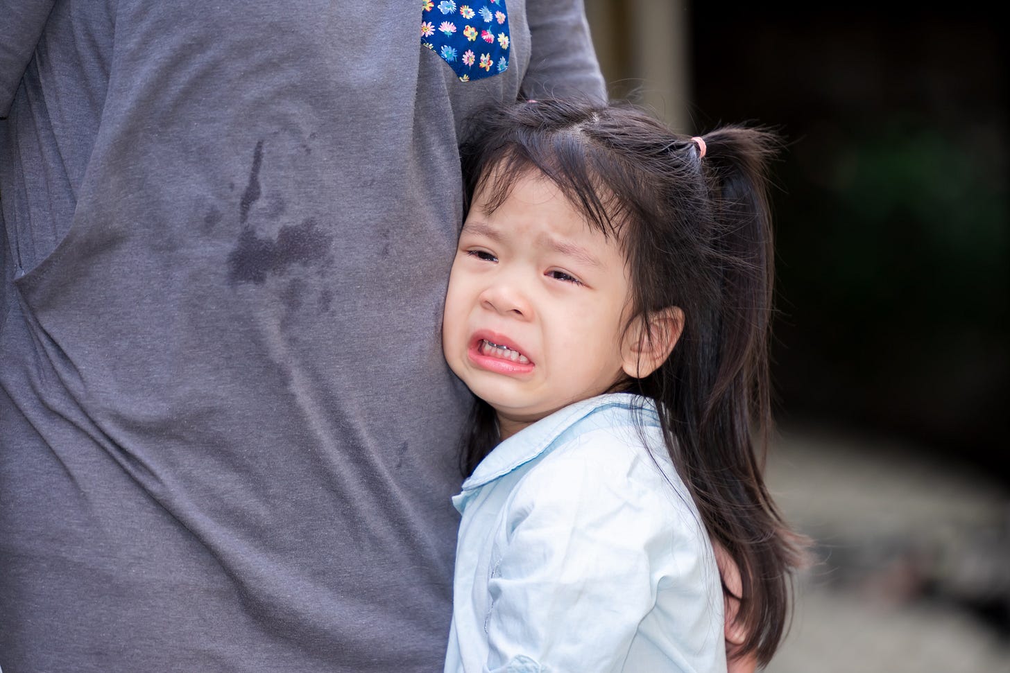 Adorable Asian girl is crying with tears on her cheeks. Child rested on her mother's belly. Children is in pain from heartache. A 4 years old wear light blue shirts.