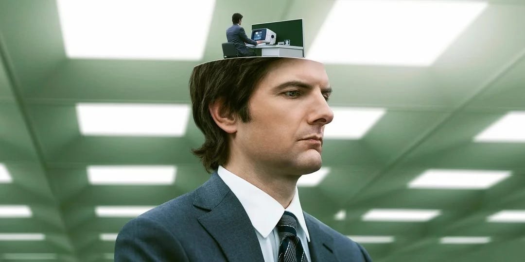 Adam Scott in the promo shot for the Apple TV Plus show Severance, showing his character Mark whose head seems to be open and housing a miniaturised version of himself at a desk