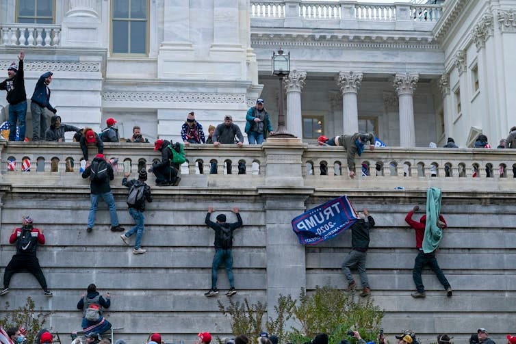 people carrying a Trump flag climb the walls of the capital