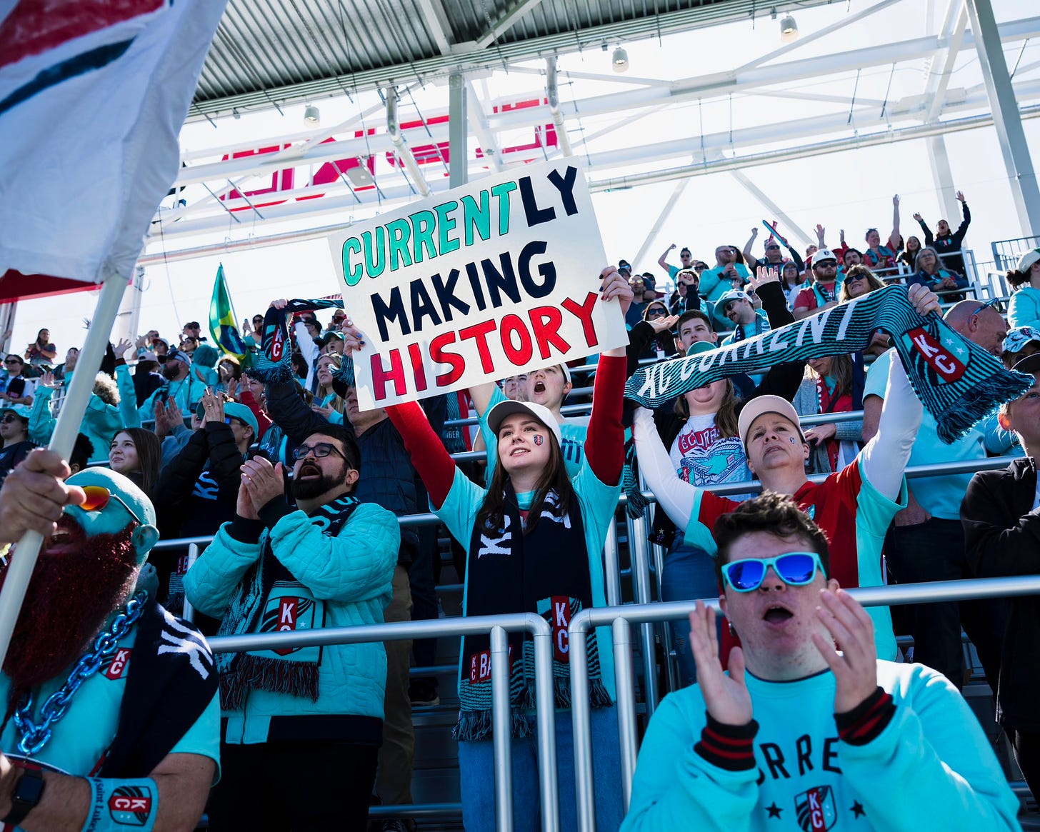 Photo of our fans with one holding up a sign that says “Currently making history”