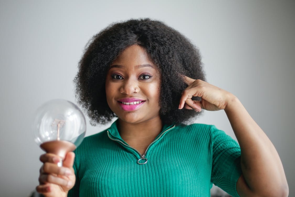 Free Positive young African American lady holding light bulb in hand on gray background Stock Photo