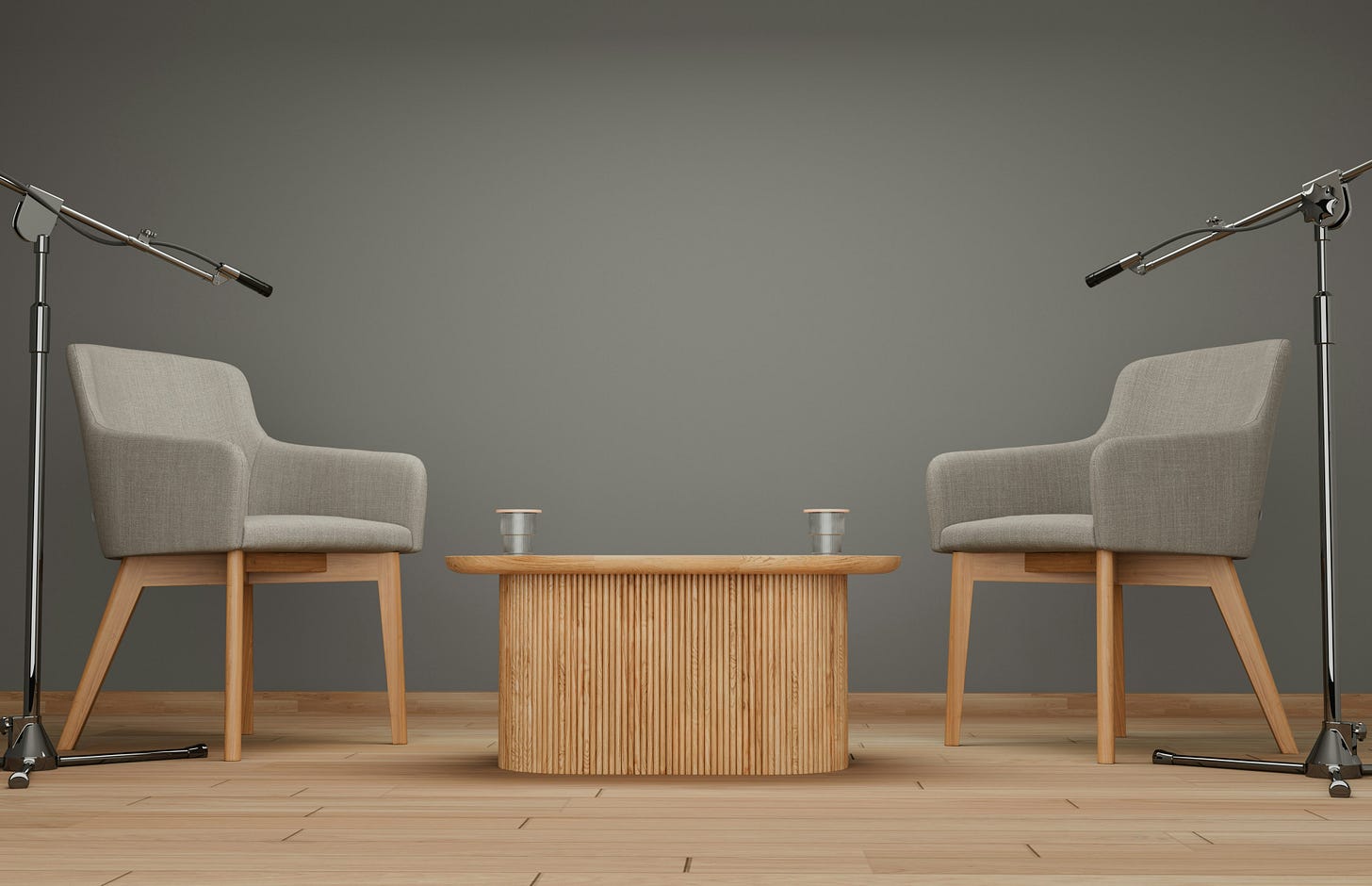 two brown chairs on either side of a wood table with microphones pointing down toward them.