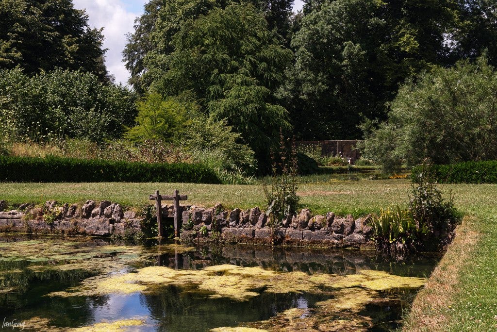 A large pond framed by gardens and a stone wall, part of the west front view at Dyrham Park, Wiltshire, UK