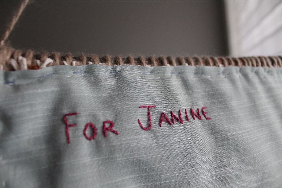 light blue fabric with "FOR JANINE" stitched on it in dark purple