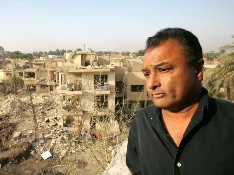 Kim Sengupta in Baghdad, standing with a concerned look on his face in front of destroyed and part-destroyed three-storey buildings