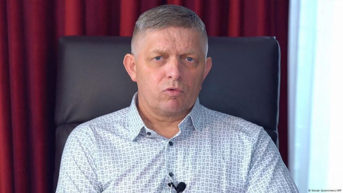 Slovak Prime Minister Robert Fico sits on a high leather chair and speaks into a microphone attached to the button panel of his shirt