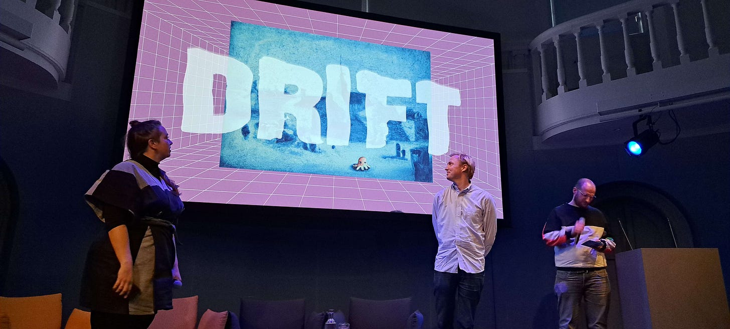 Nienke, Lieven en Hay op het podium van het Felix Meritis met op het scherm op de achtergrond het artwork van DIRFT.