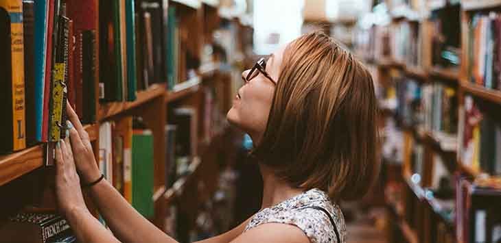 Photo of a woman looking through shelves of books in a library.