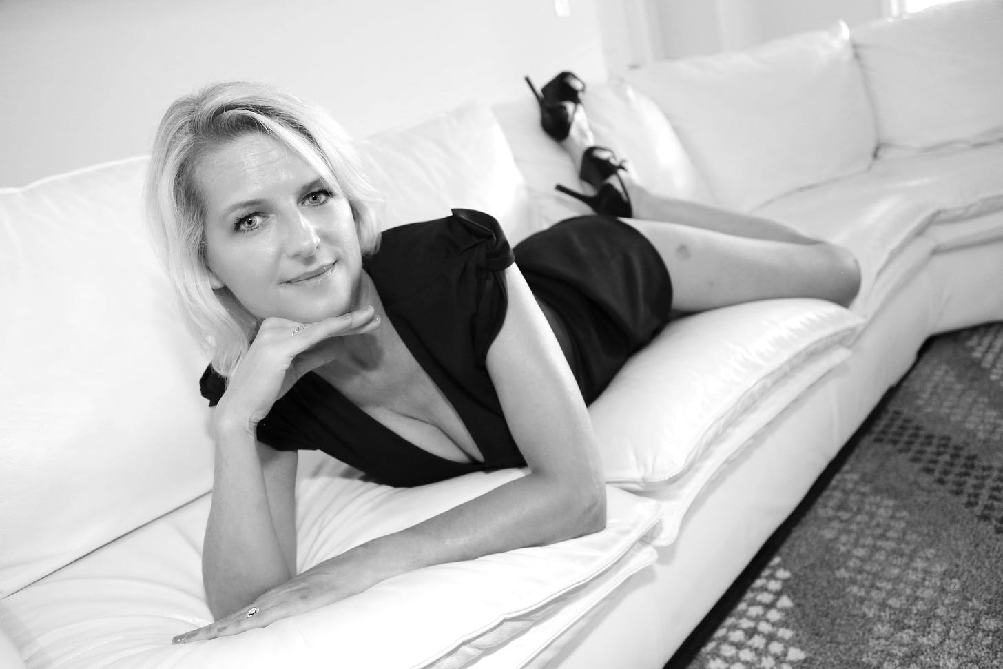 Woman in black dress lying on white sofa, black and white photo