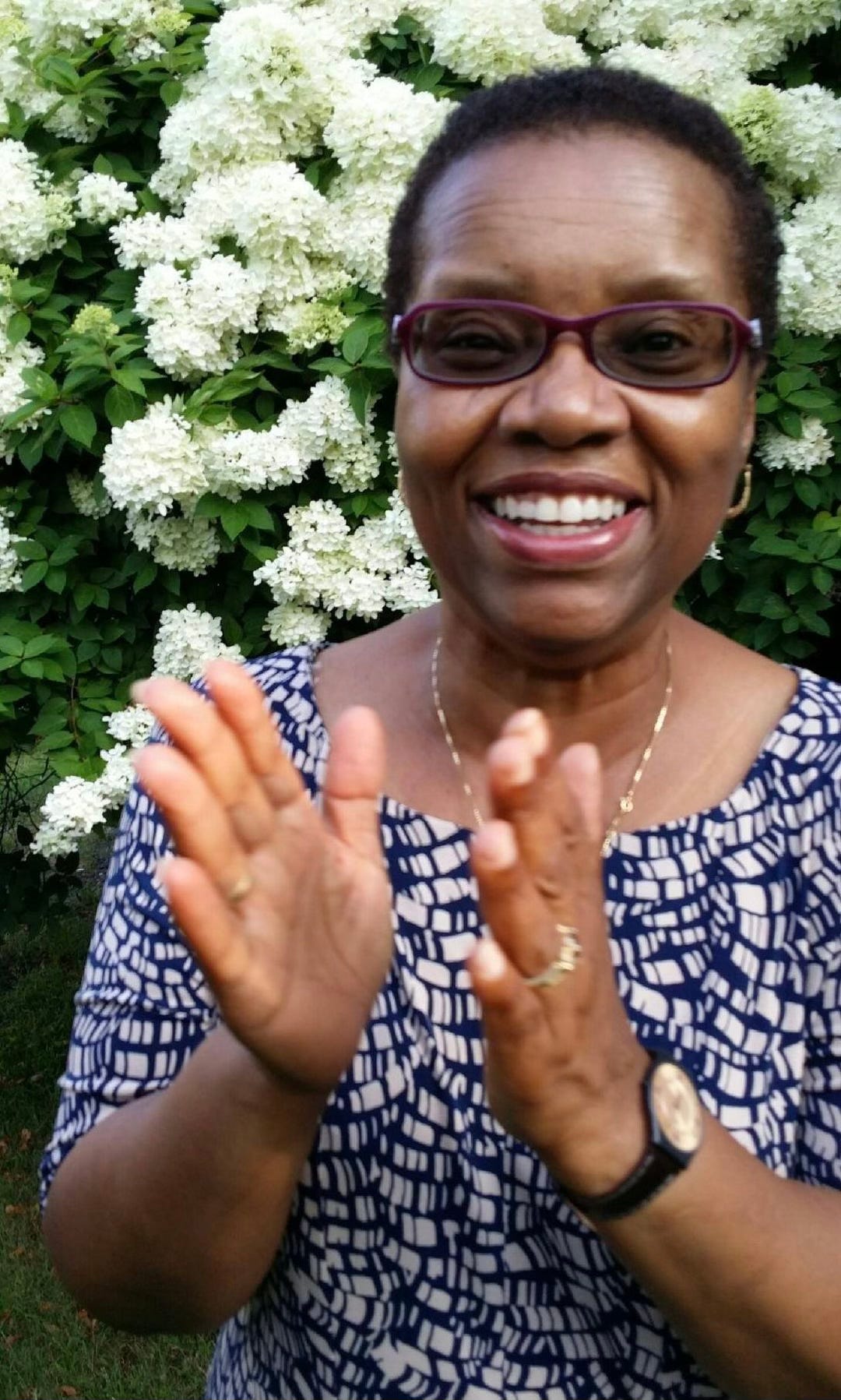 Portrait of black woman smiling and clapping her hands against backdrop of white hydrangeas.