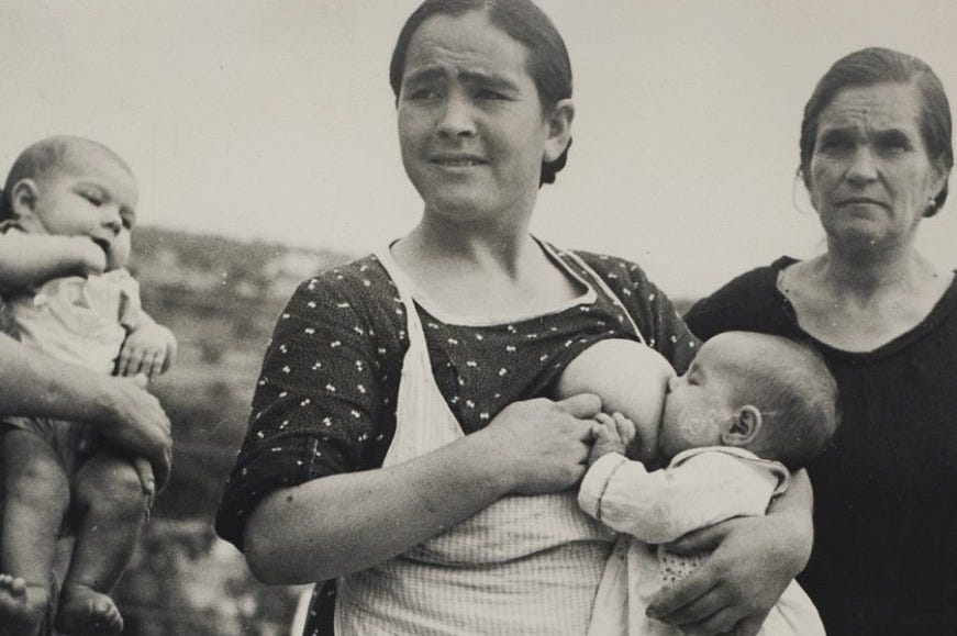 Due donne, una sullo sfondo e una in primo piano che allatta un neonato. Sulla sinistra un altro neonato viene tenuto in braccio da una figura che non è visibile. La foto è in bianco e nero e risale alla guerra spagnola.