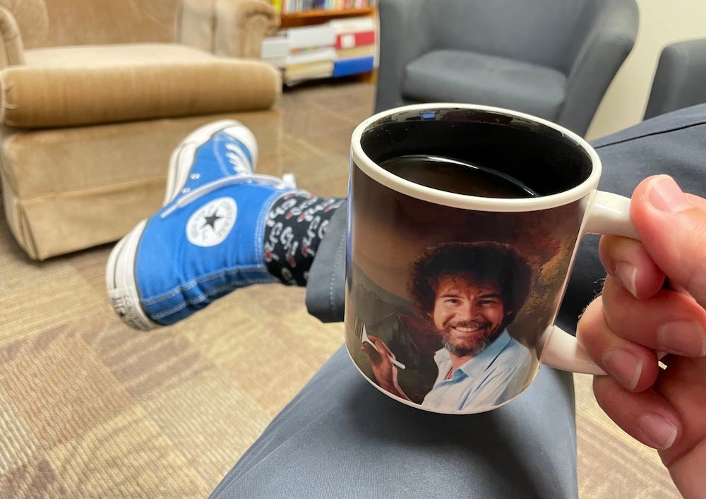 A mug of coffee with Dr. Dave's blue Converse high-tops in the background.