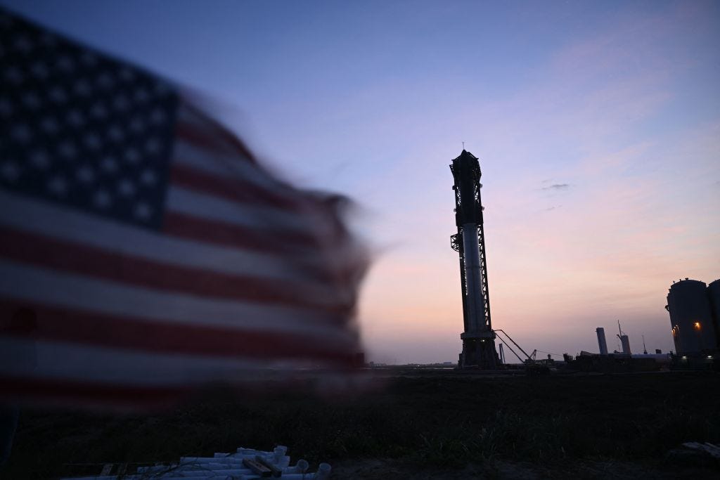 An American flag flies in the foreground of SpaceX's Starship rocket.