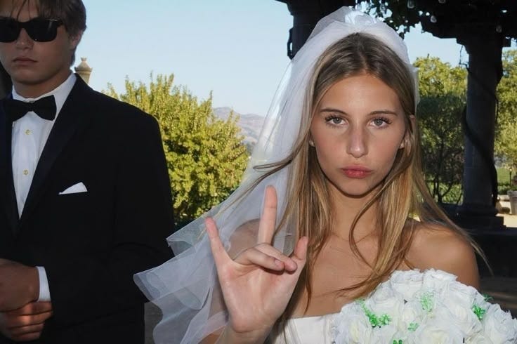 This may contain: a woman in a wedding dress making the peace sign with her hand while standing next to a man