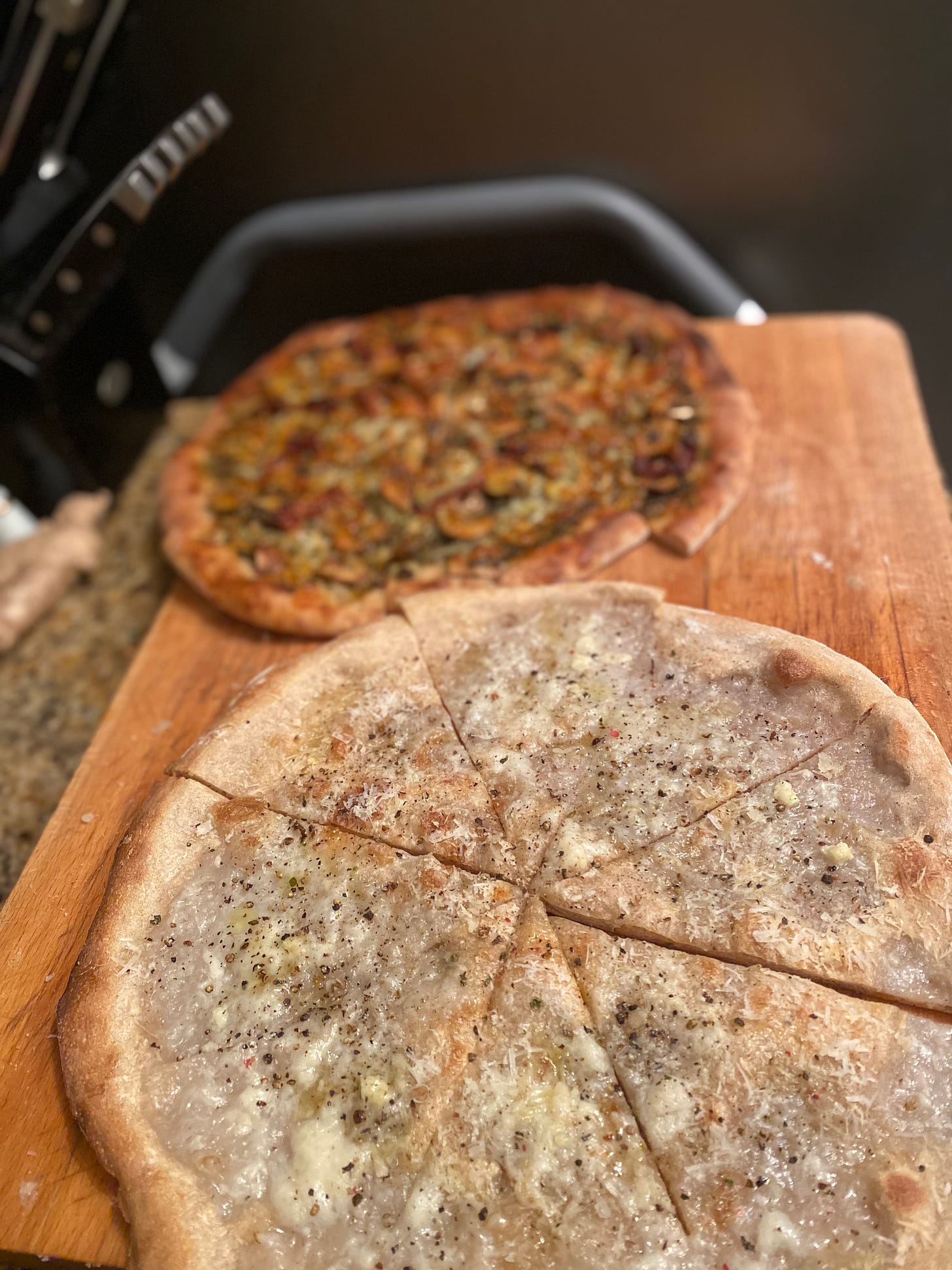 The two pizzas described above, cacio e pepe in the foreground and pesto with sun-dried tomato and mushroom in the background.