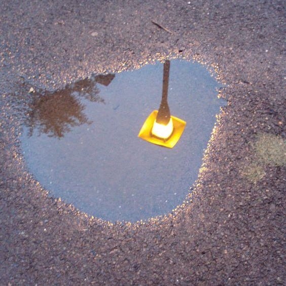 This may contain: a yellow traffic light sitting in the middle of a puddle