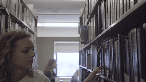 A woman searches a long bookshelf A woman searches a long bookshelf