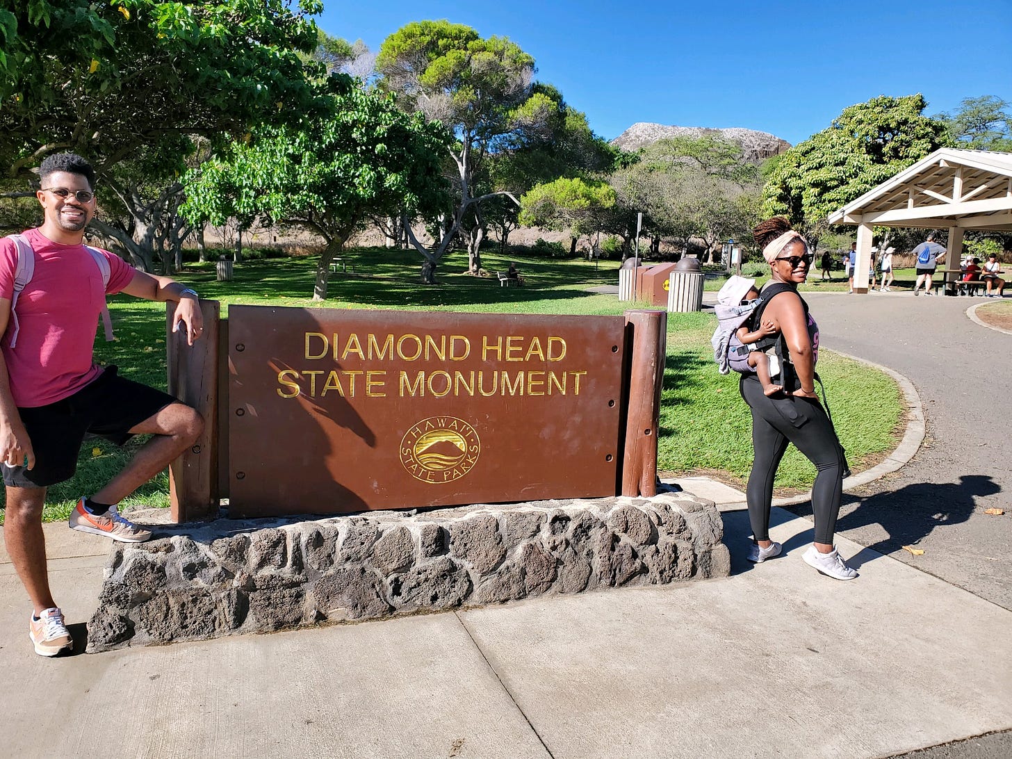 Black family posing in front of sign that reads Diamond Head State Monument in Honolulu, Hawaii.