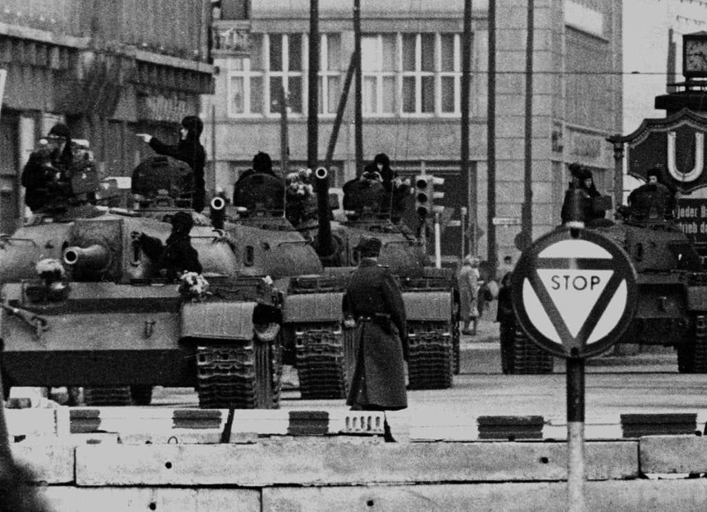 A black and white photo of Russian T-55 tanks viewed from the front. A low concrete block wall marks the demarcation line with West Berlin. A stop sign stands between the Russian hordes and the free West. It was presumably doubts over the efficacy of the Stop sgn that led to the development of tactical nuclear weapons.