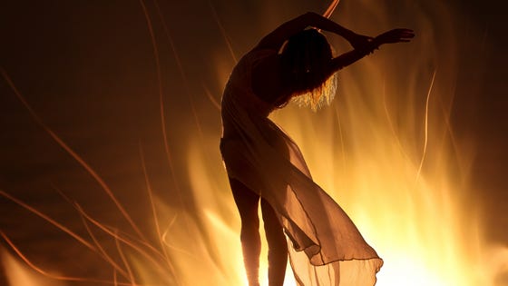 Silhouette of a woman dancing before a blaze, her semi-sheer skirts are back-lit