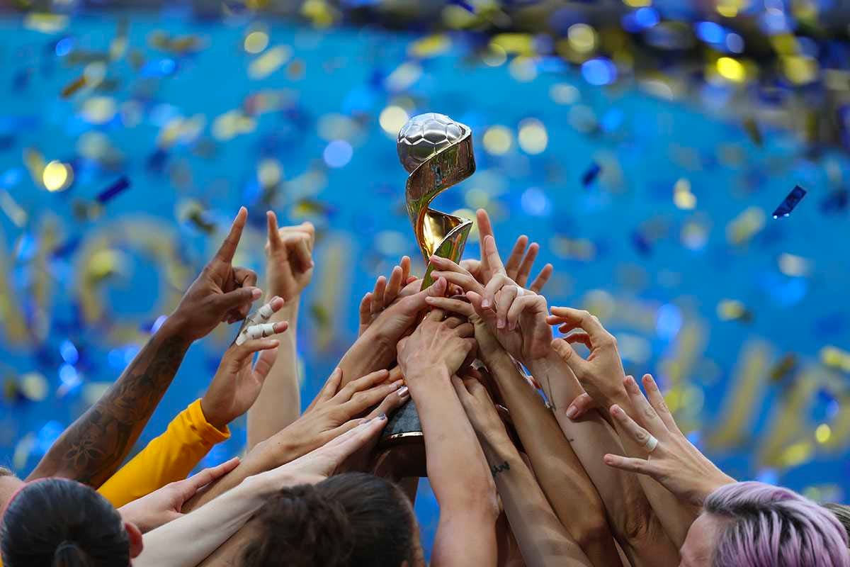 The many hands of the US womens football team reaching up towards the world cup trophy.